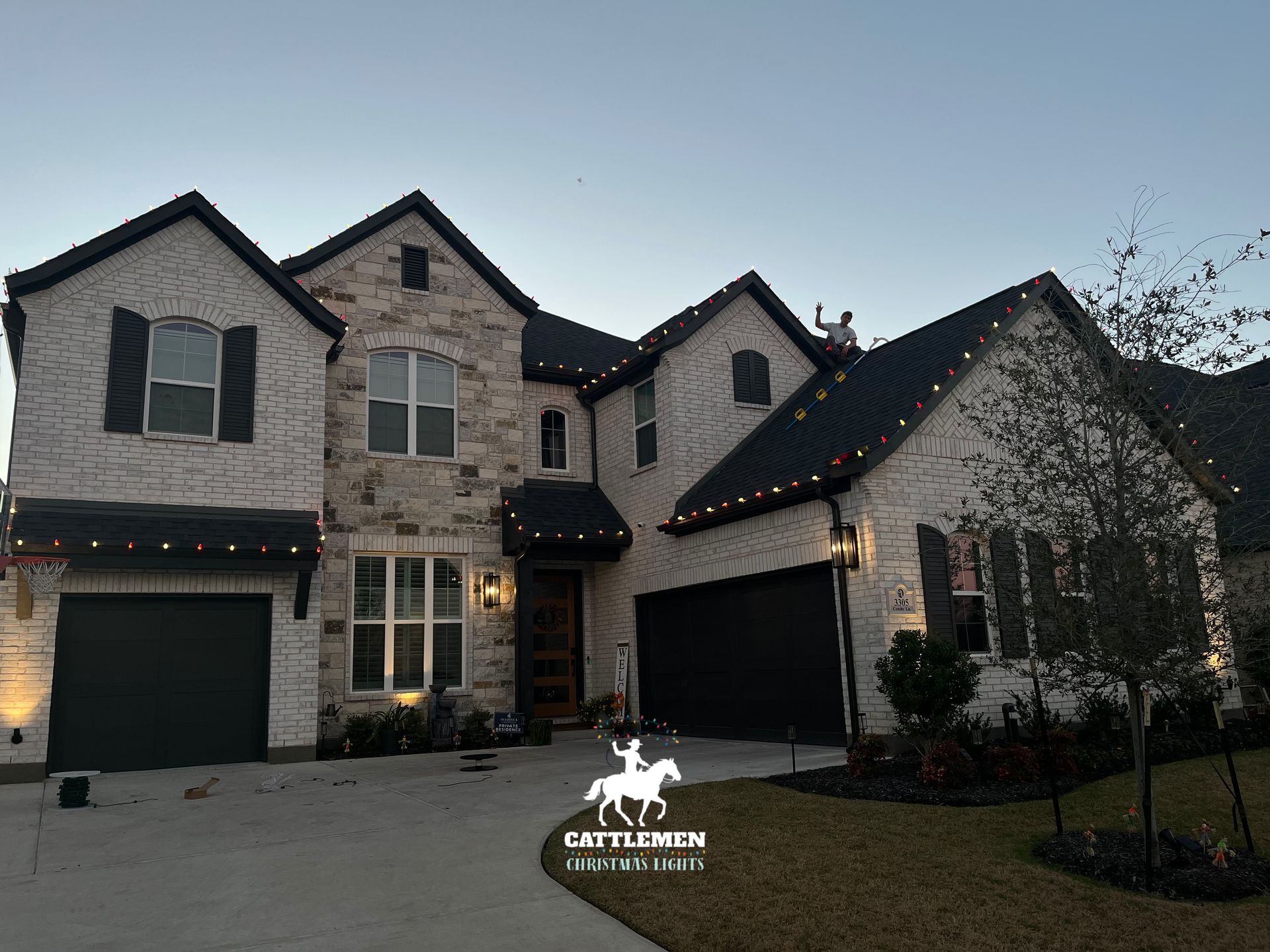 Two-story brick house at dusk with lit string lights and a double garage