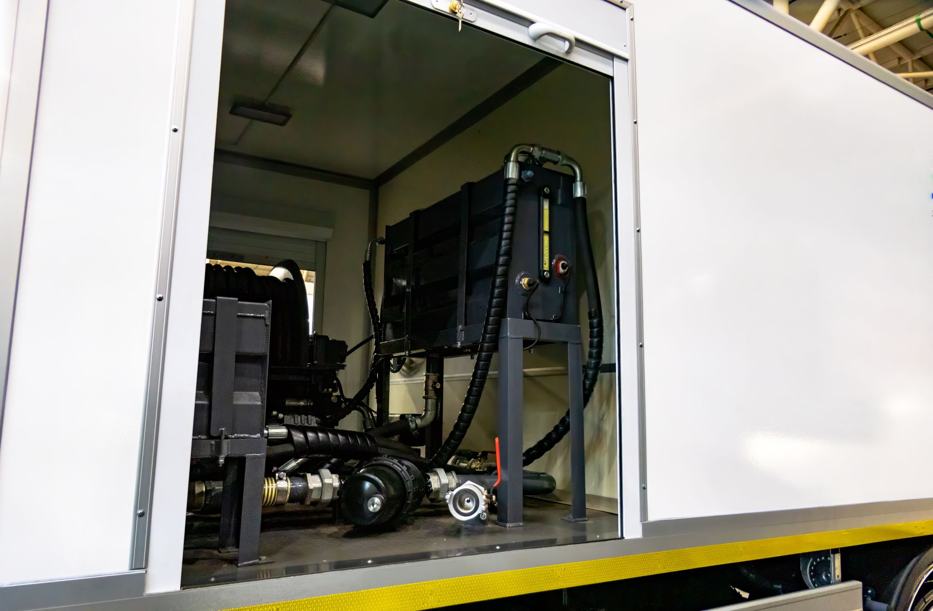 Interior view of a white mobile unit with machinery, pipes, and tanks visible through an open doorway.