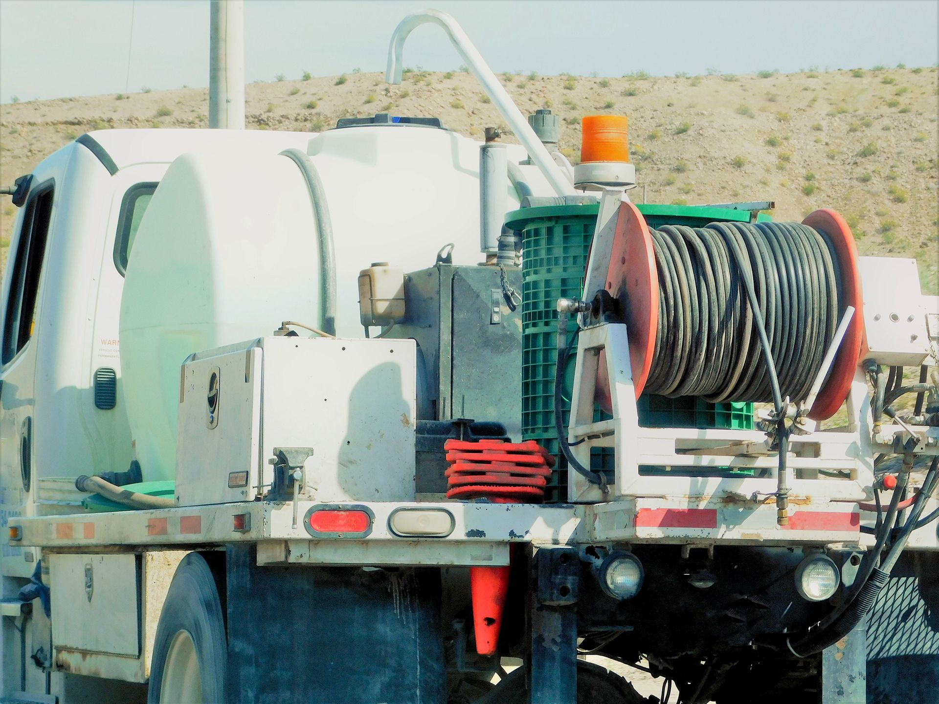 Truck bed with a large reel of cable, water tank, and equipment; set in a desert.