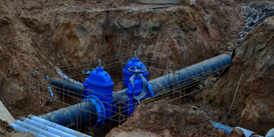 Blue valves attached to large pipes in a construction site trench.