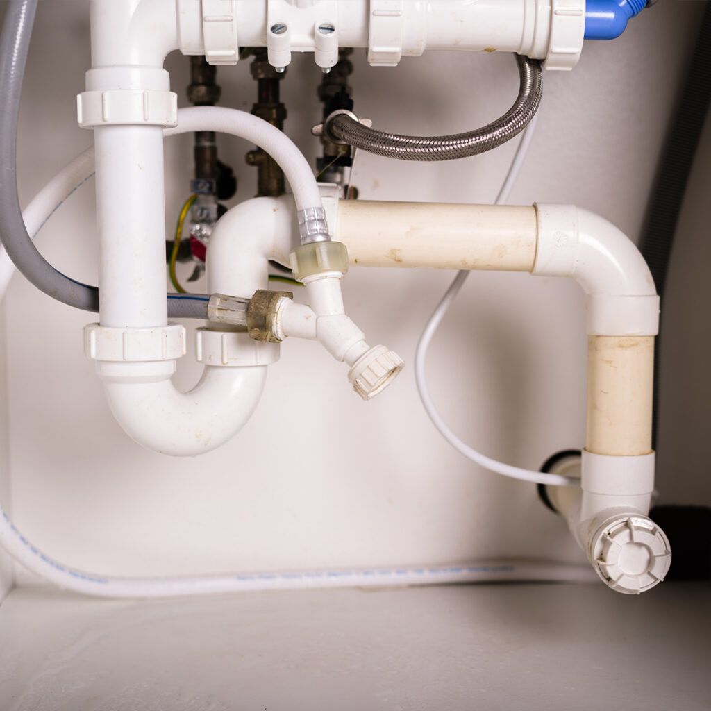 White plumbing pipes and fittings under a sink.
