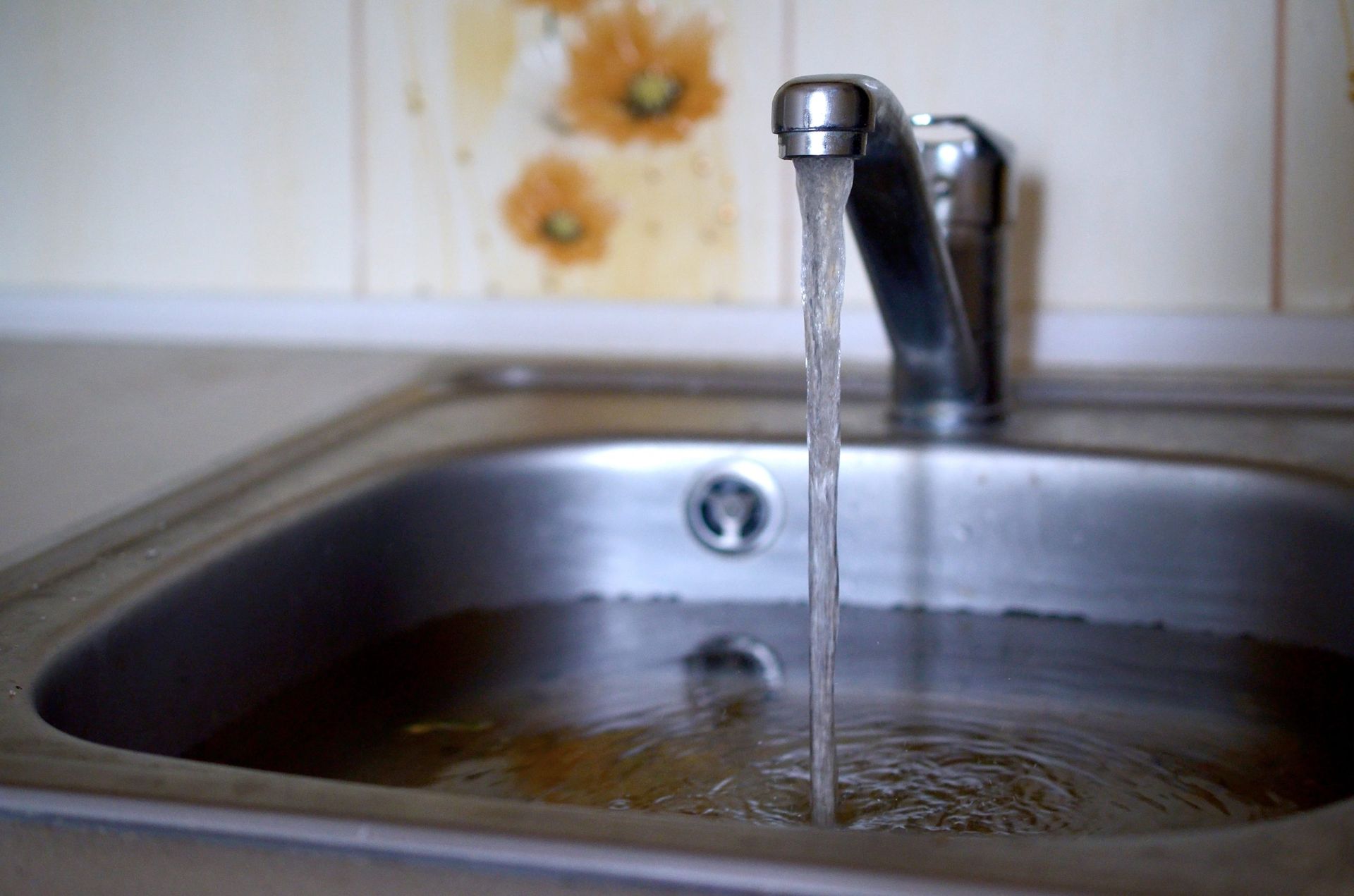 Water flowing from a silver faucet into a partially filled stainless steel sink.