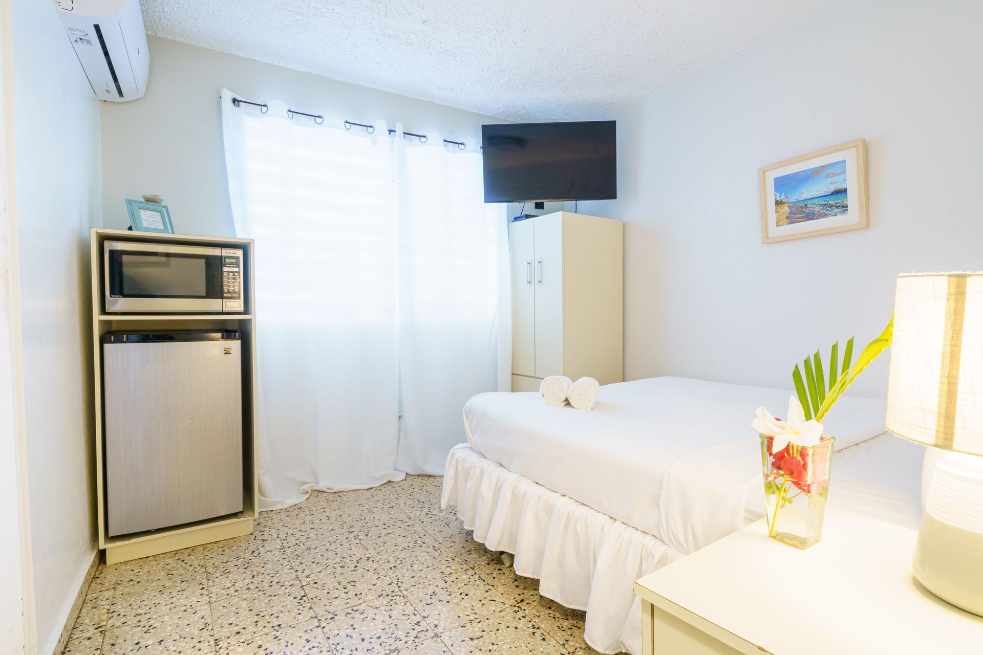 A bedroom with a bed , television , microwave and refrigerator.