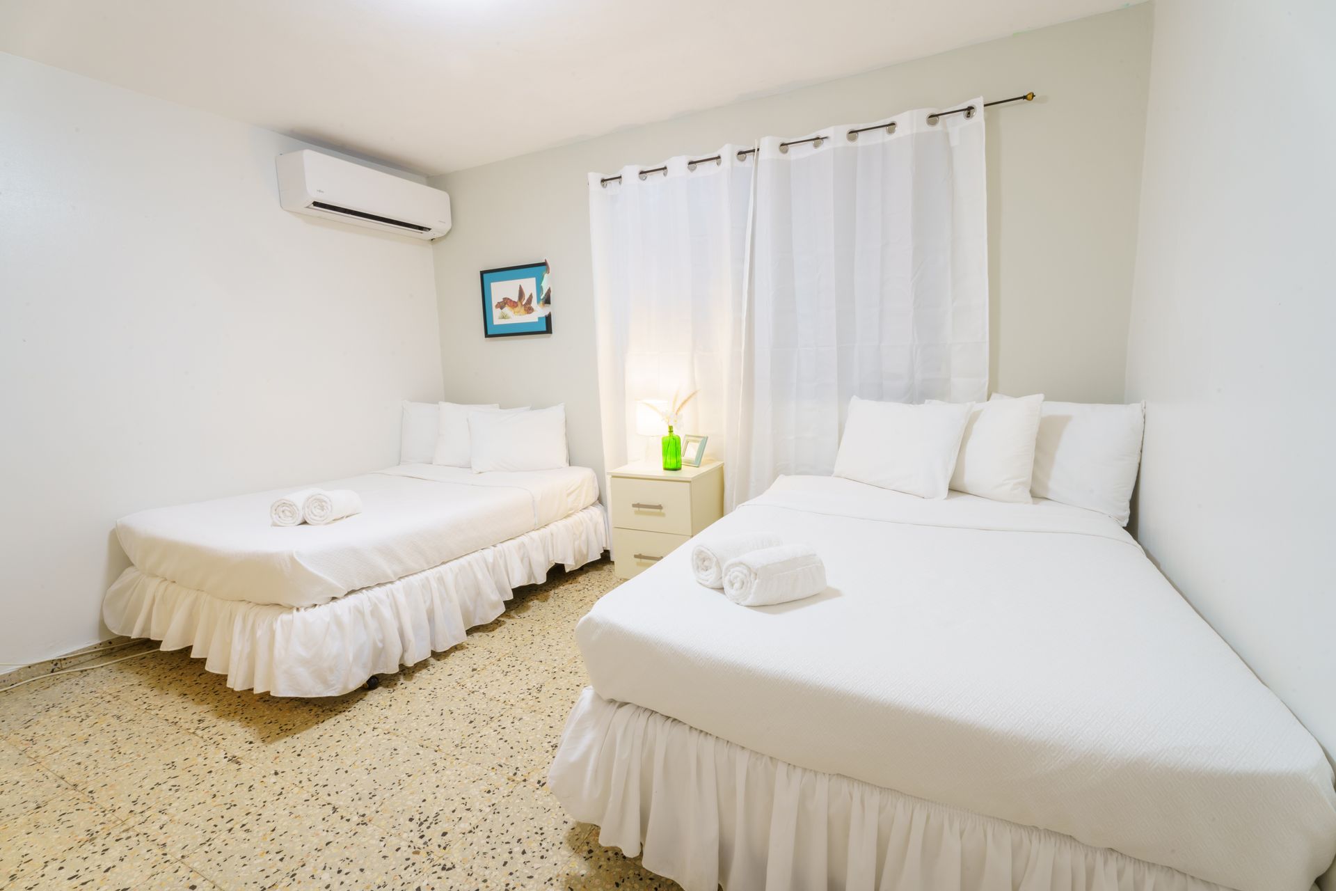 There are two beds in the room with white sheets.