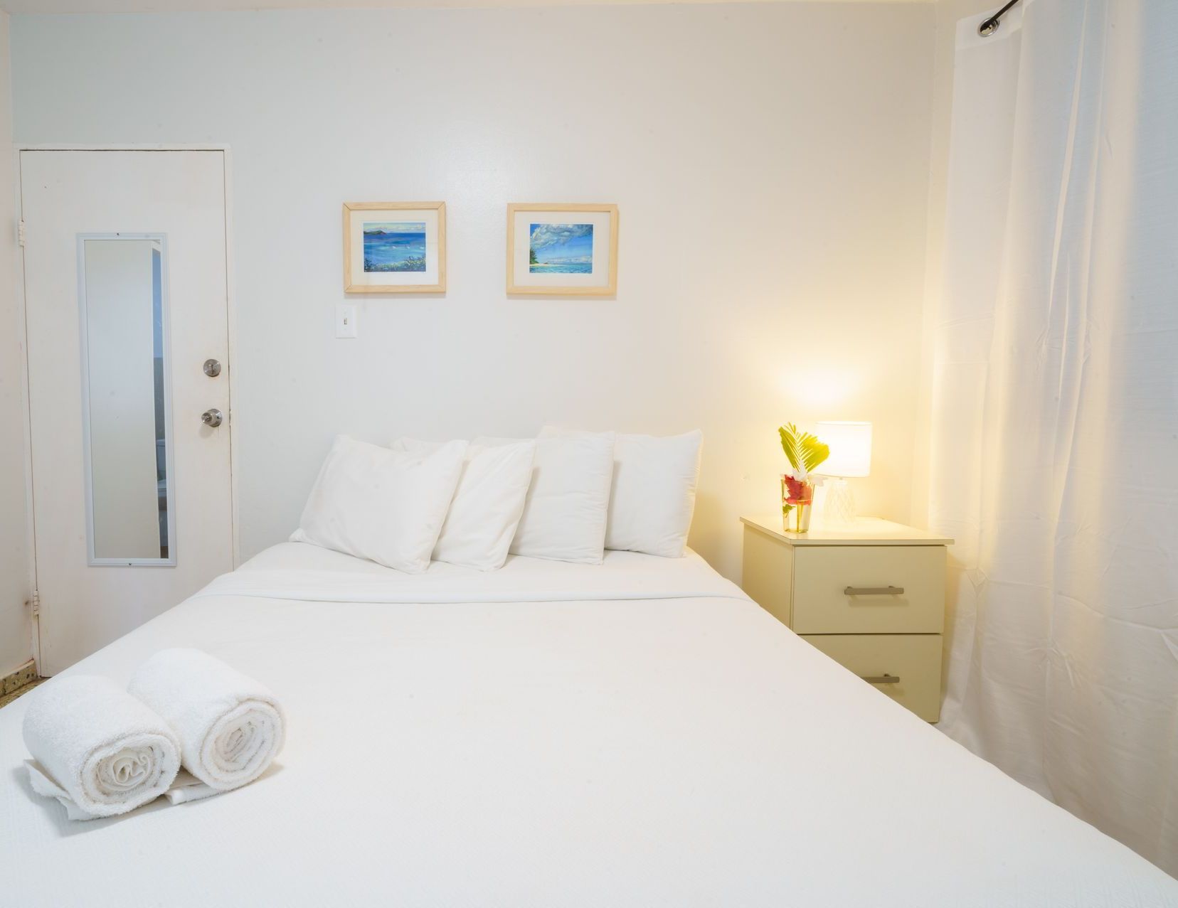 A bedroom with a bed , nightstand , mirror and two pictures on the wall.