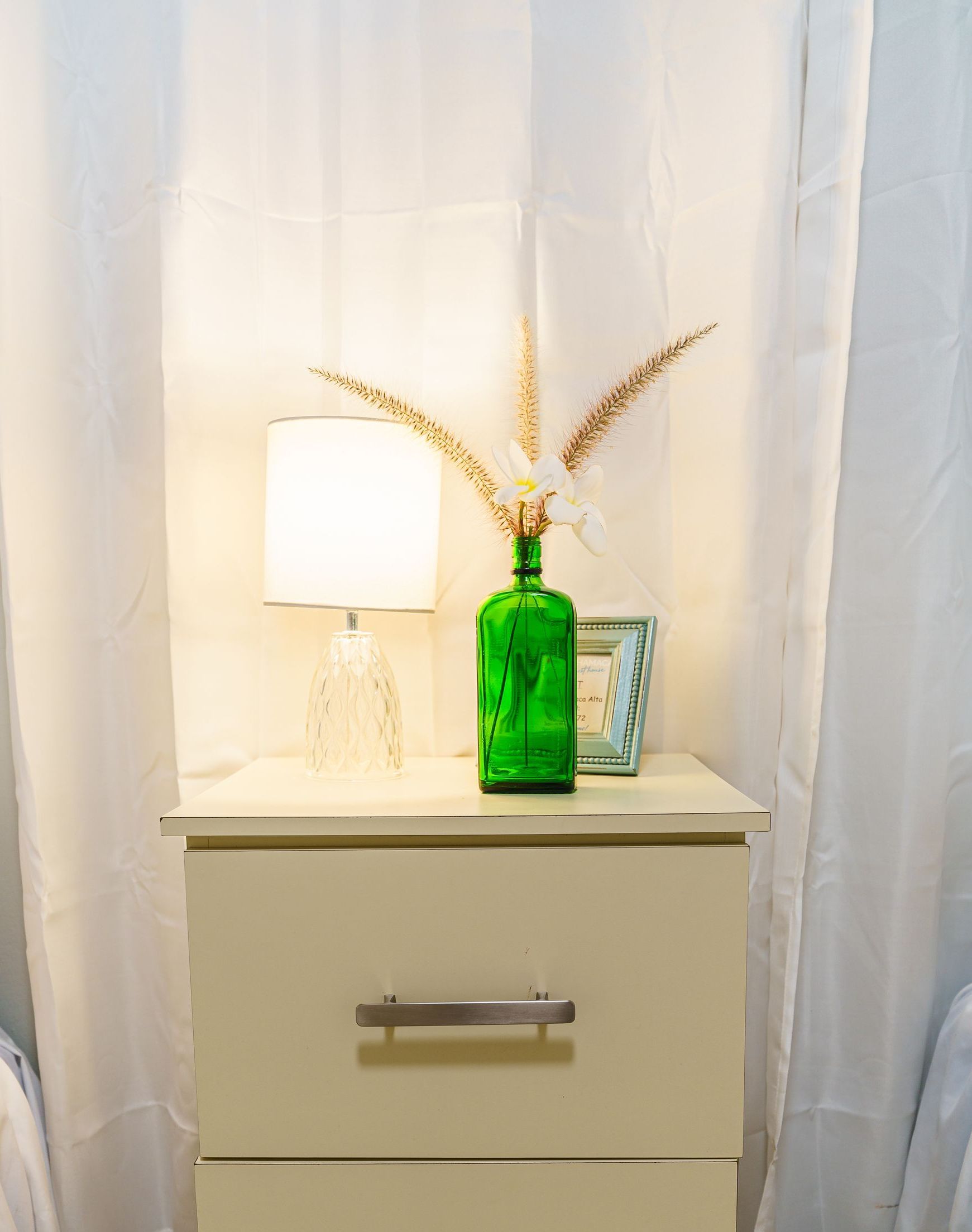 A nightstand with a green vase and a lamp on it
