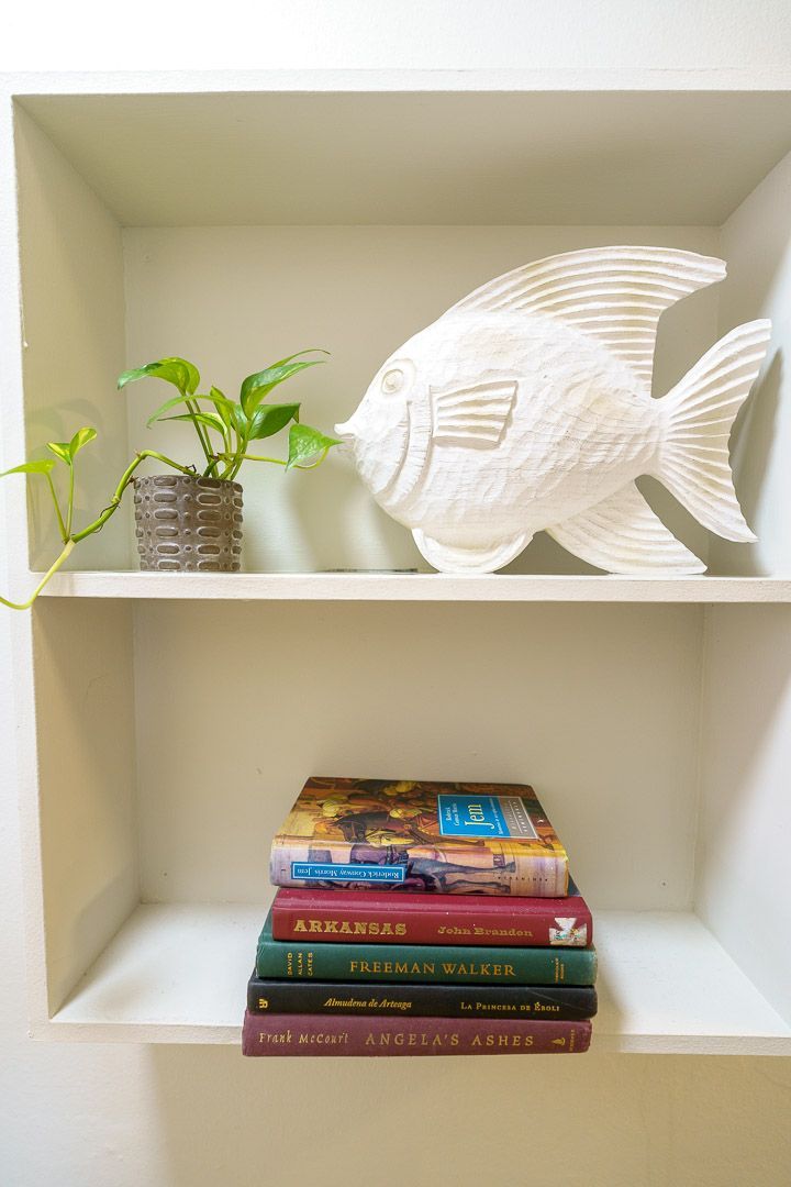 A shelf with a stack of books and a fish on it.