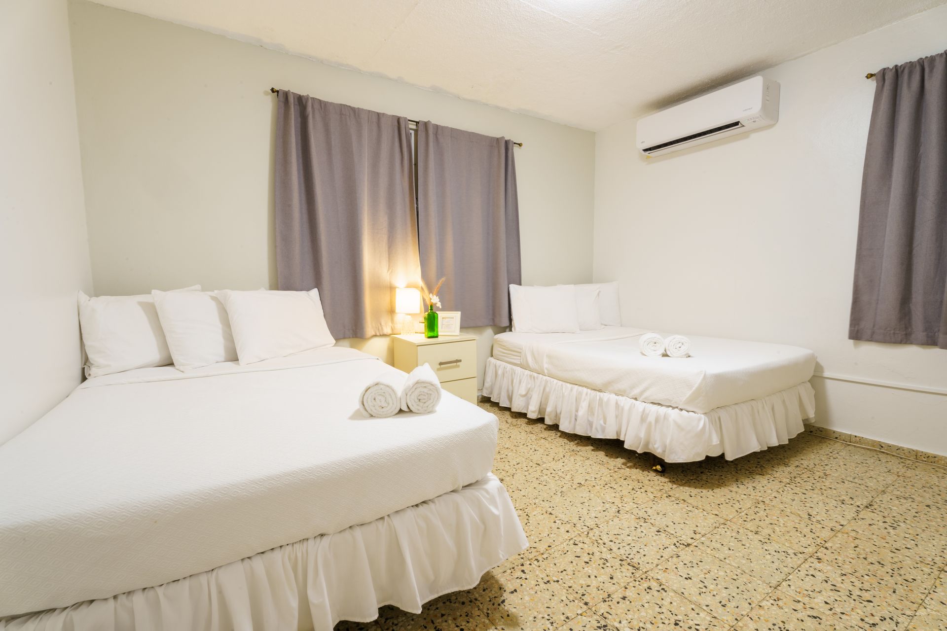 A hotel room with two beds and two windows.