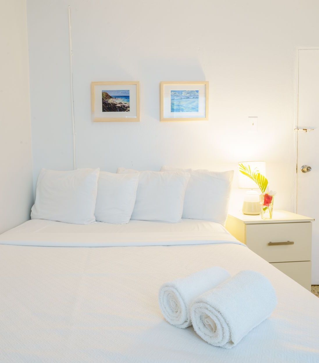 A bedroom with a bed , nightstand , and two pictures on the wall.