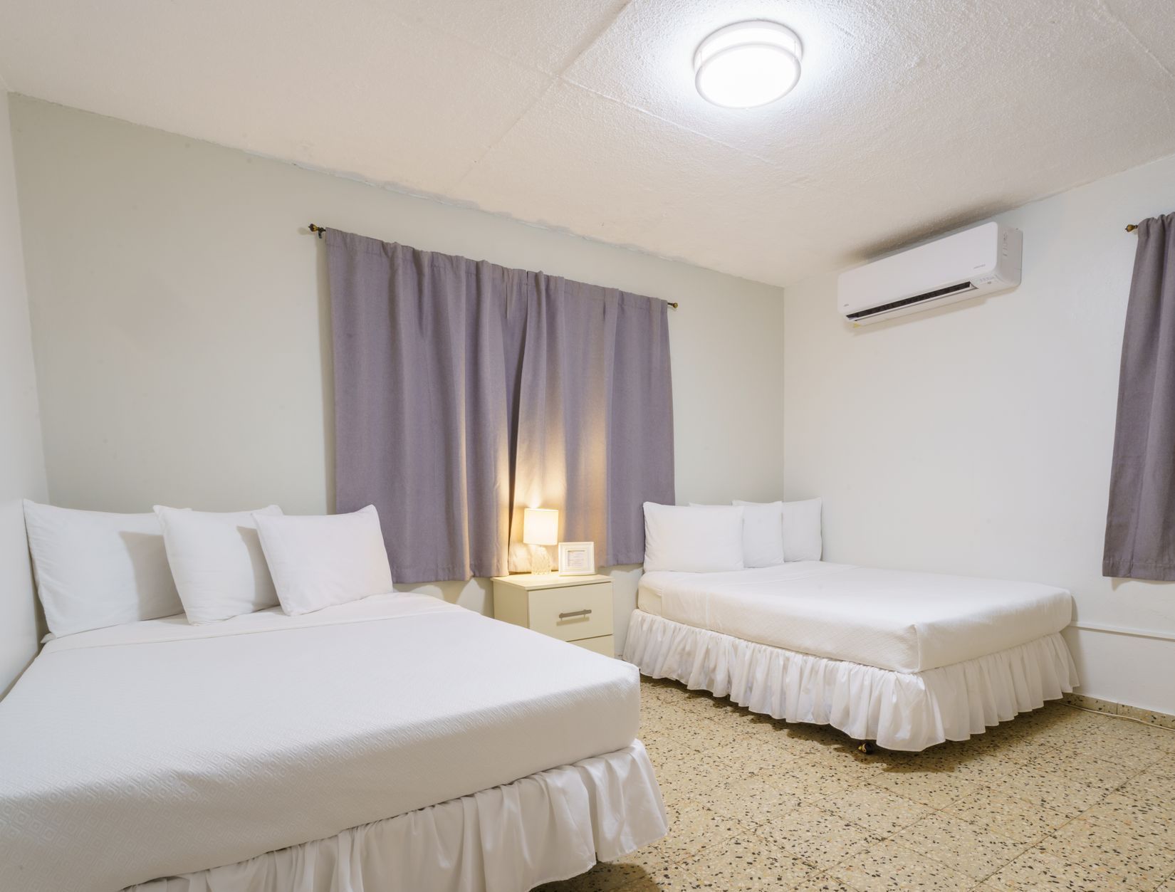A hotel room with two beds and purple curtains
