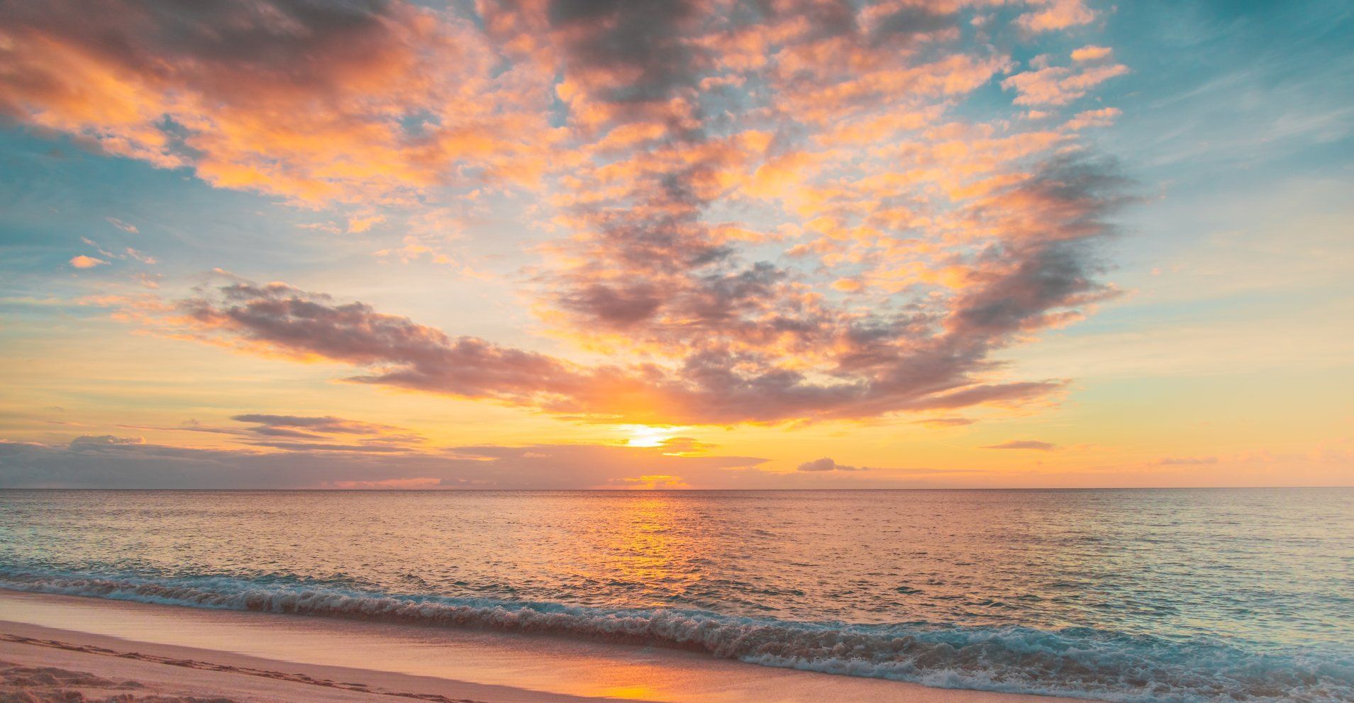 The sun is setting over the ocean and the clouds are changing colors.