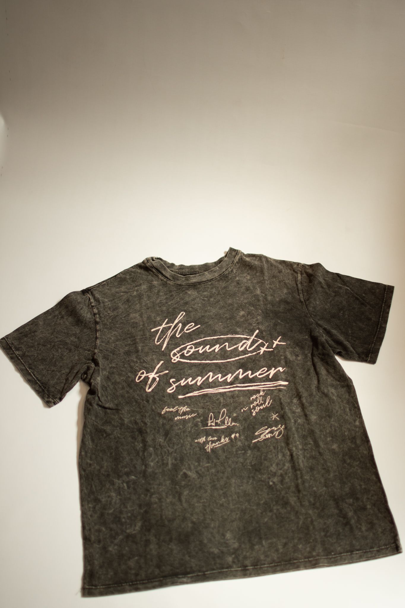 Camiseta gris oscuro con texto rosa descolorido en la espalda, en ángulo sobre una superficie blanca.