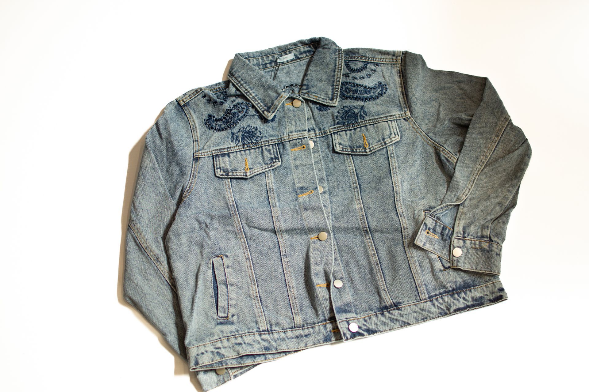 Chaqueta vaquera azul con detalles bordados sobre fondo blanco.