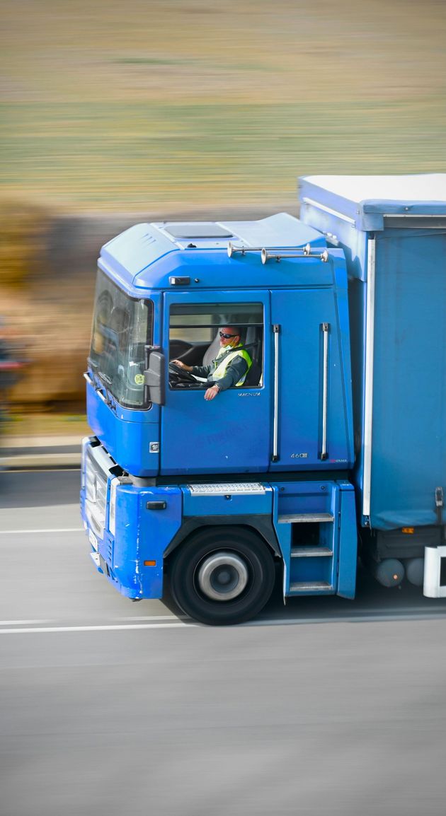 Blue semi-truck driving on a road, blurred background suggesting motion.