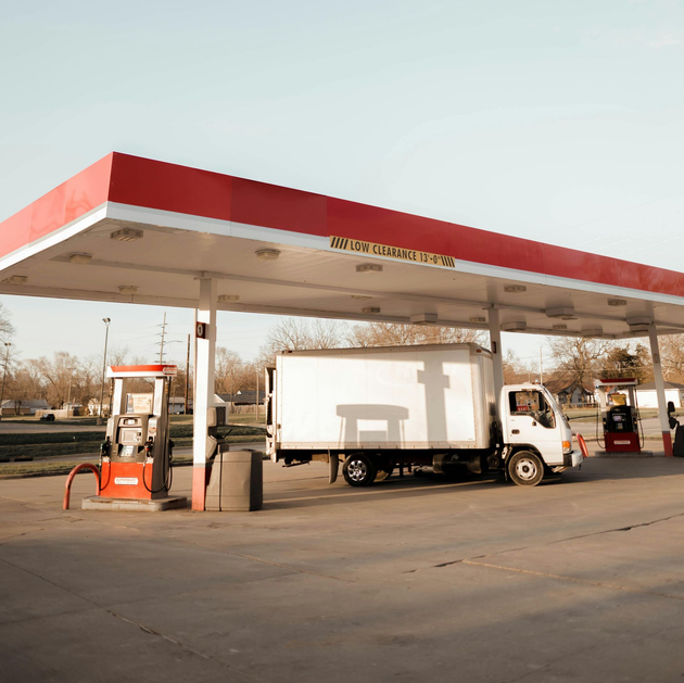 Truck parked under a red-and-white gas station canopy beside fuel pumps