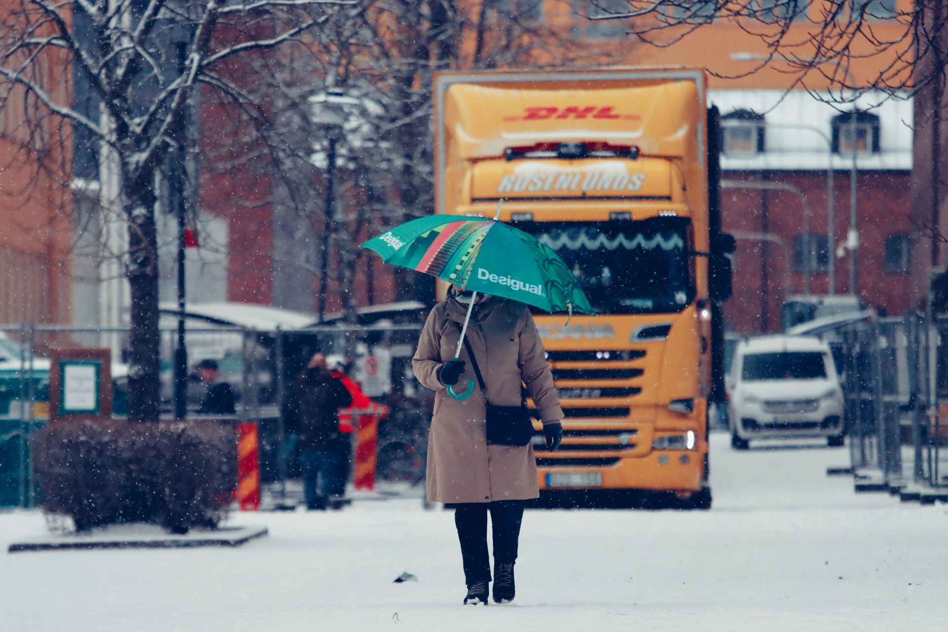 Person with green umbrella walking in snowy street toward a yellow truck