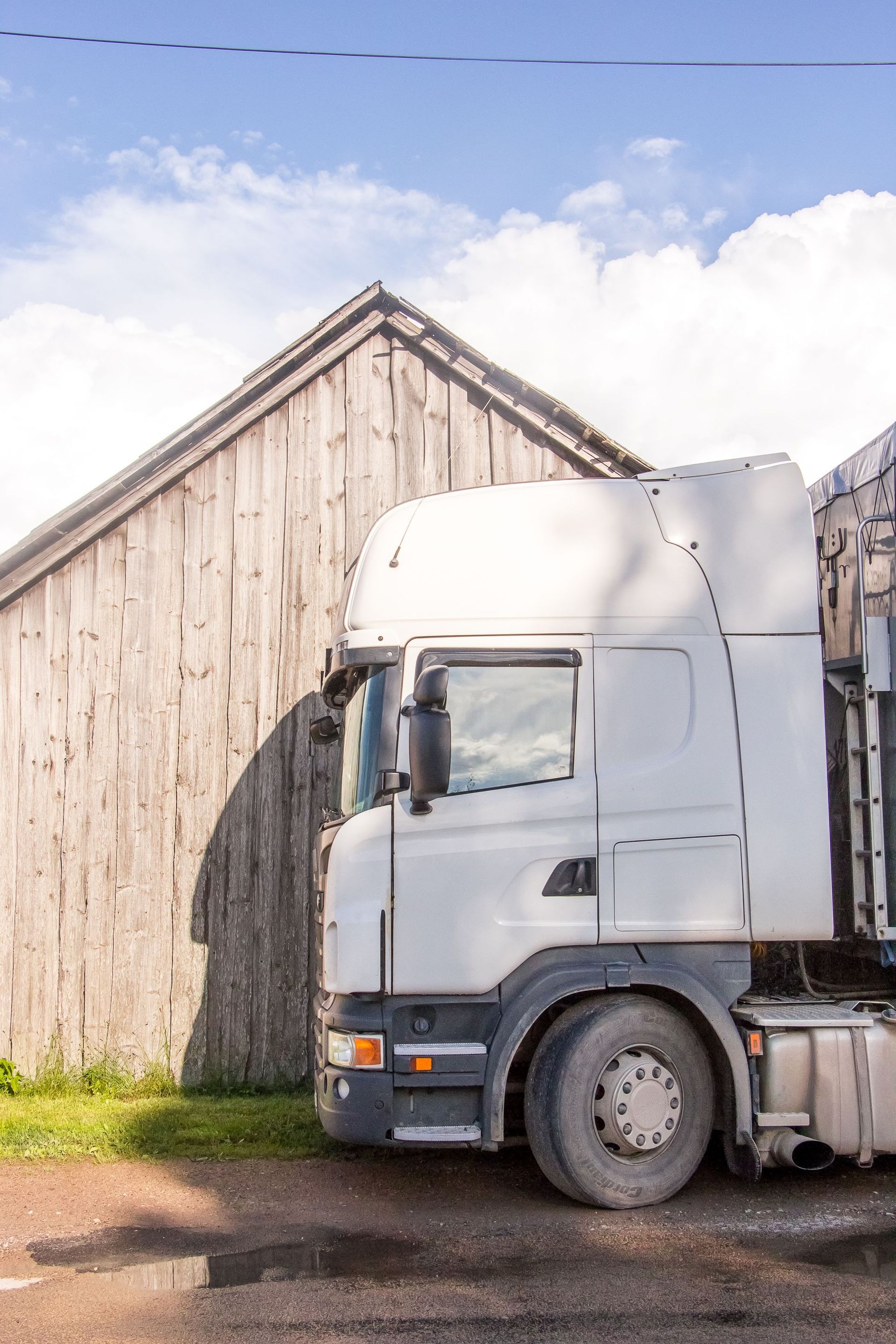 White semi-truck parked beside a weathered wooden barn under a blue sky