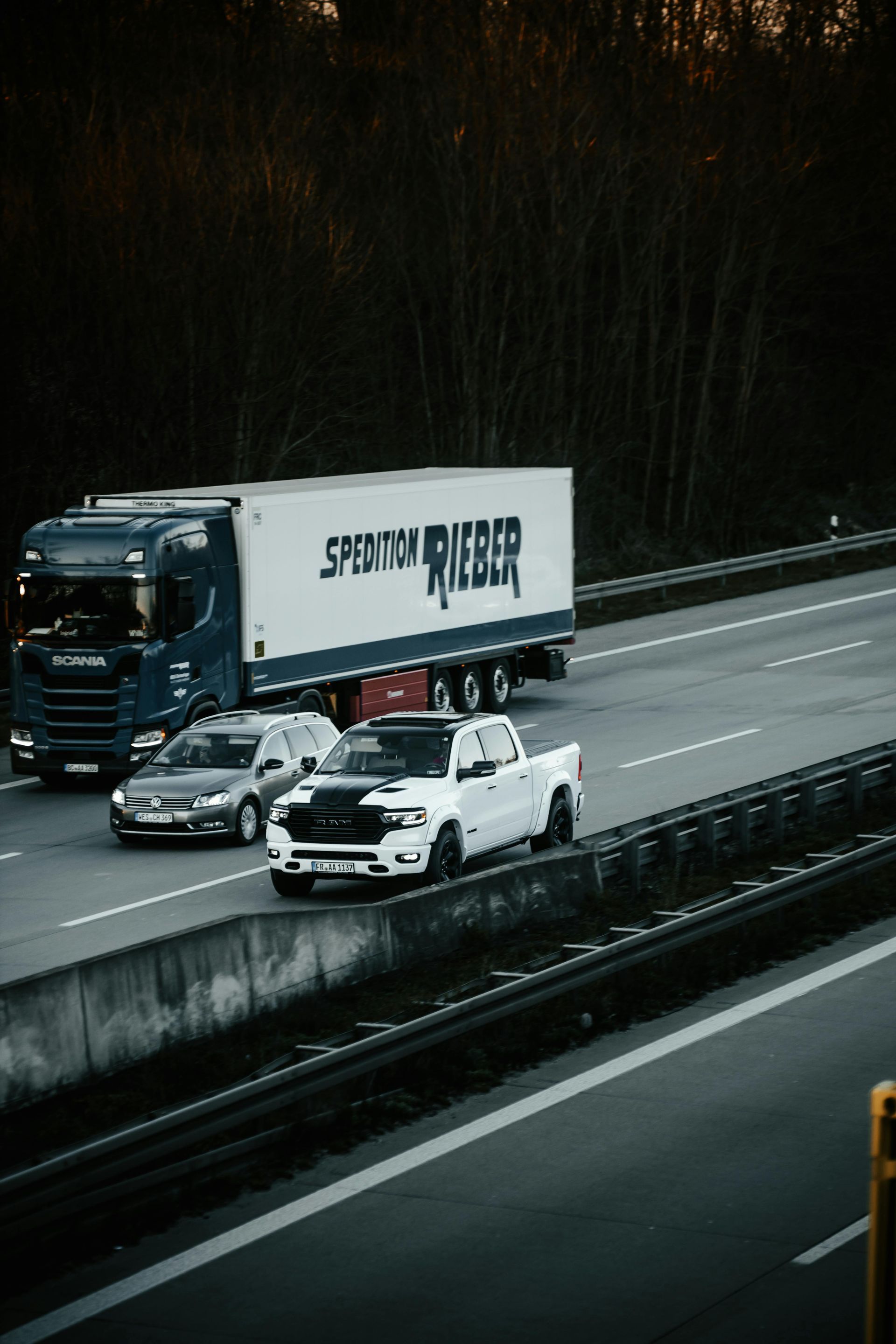 White pickup and silver car beside a semi-truck on a wet highway in a rainy forested area