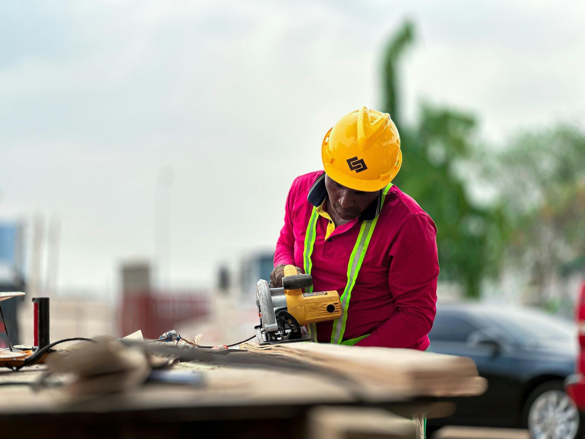 Worker in yellow hard hat using a power tool at an outdoor construction site