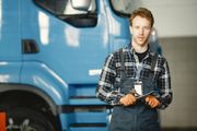 Mechanic holding a wrench in front of a blue truck in a garage