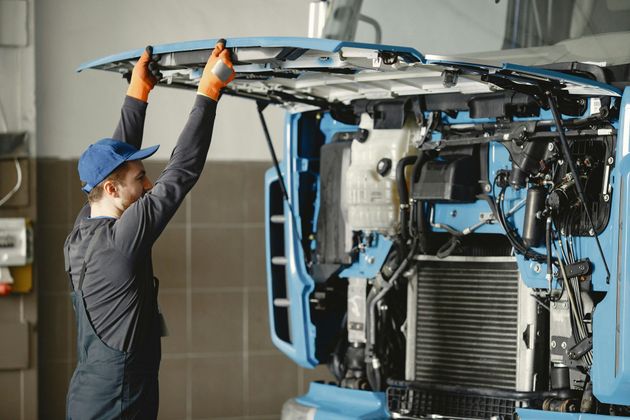 Mechanic in blue cap working on the front of a blue bus in a garage