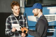 Two mechanics reviewing paperwork in a garage, with a truck in the background.