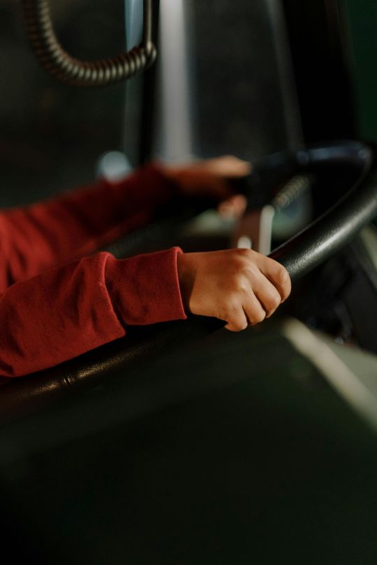 Hands in a red sleeve gripping a steering wheel in a dark vehicle interior