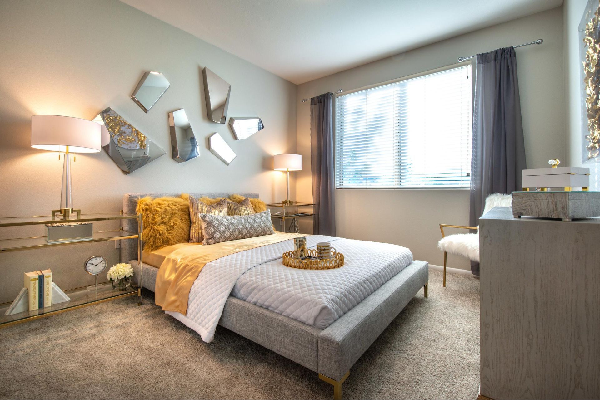 Modern apartment bedroom with a low bed, mirrored wall art, and window blinds.