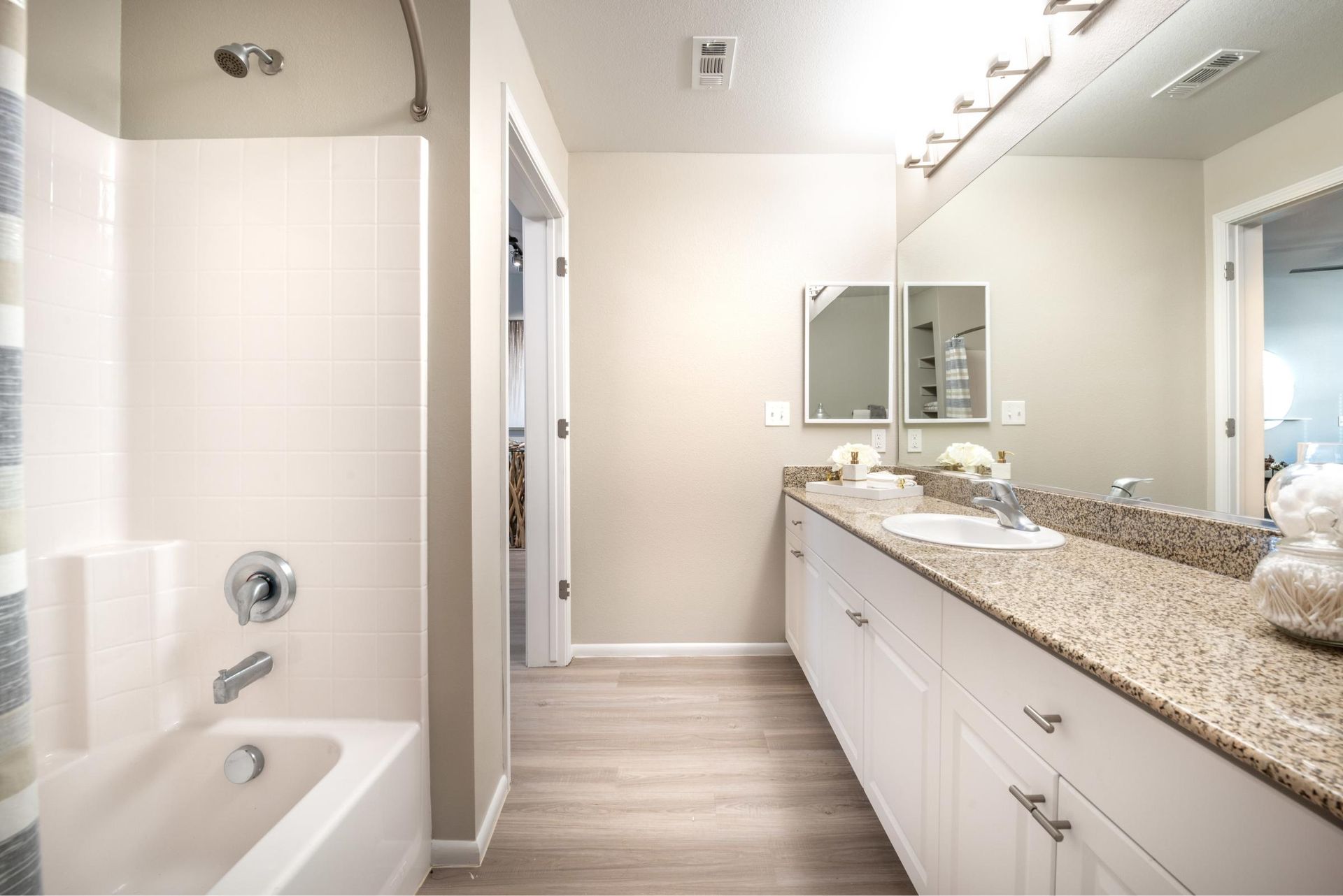 Bathroom with double vanity, granite counter, large mirror, and shower/tub.