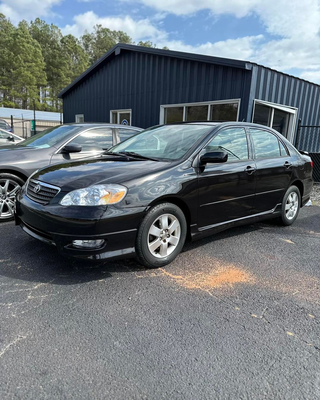 A black toyota corolla is parked in front of a building.