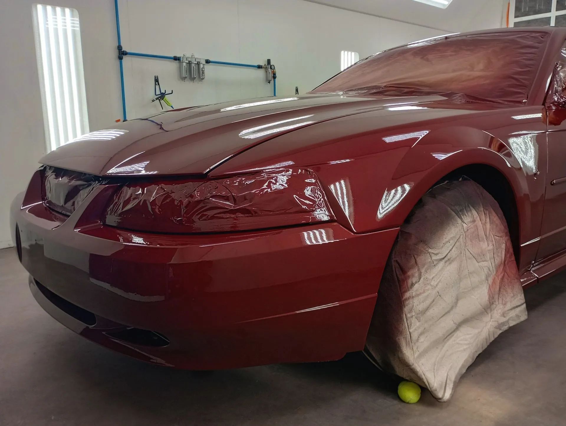 Maroon car in a garage with a covered front wheel and a tennis ball by the tire