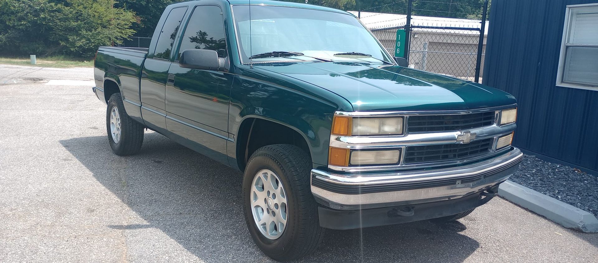 A green pickup truck is parked in front of a blue building.