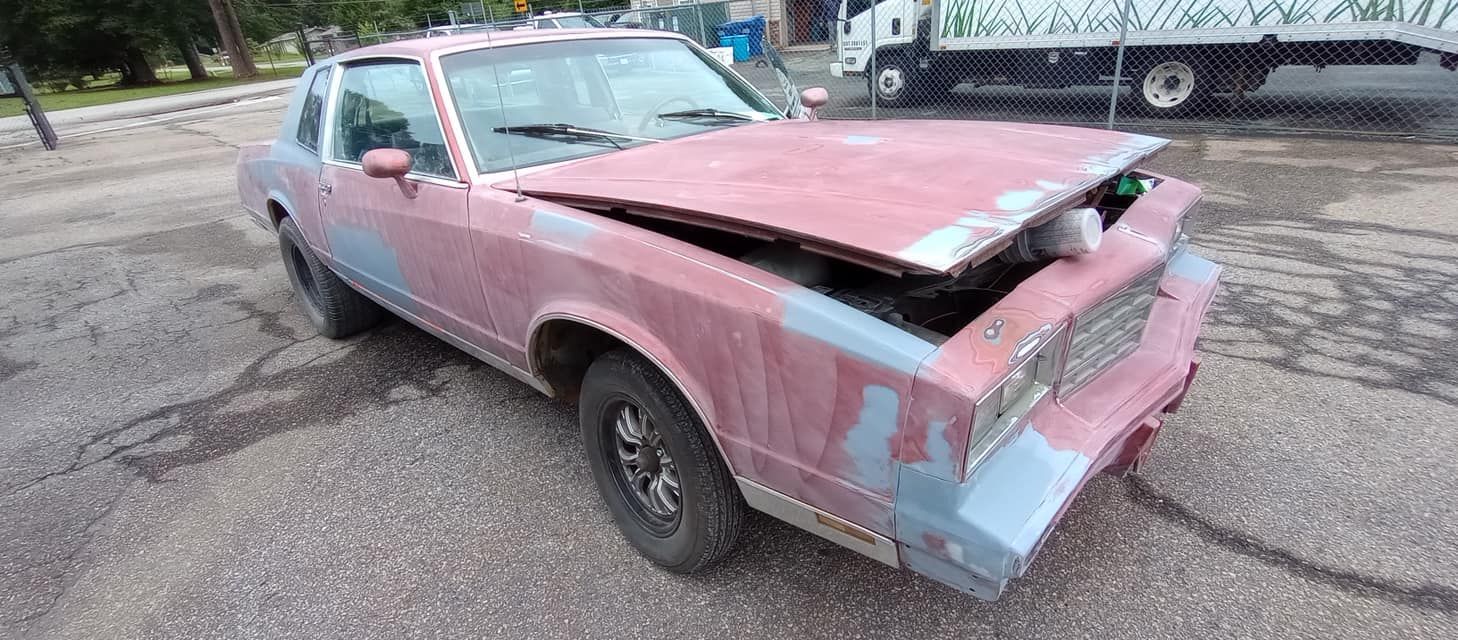 A pink car with the hood up is parked on the side of the road.