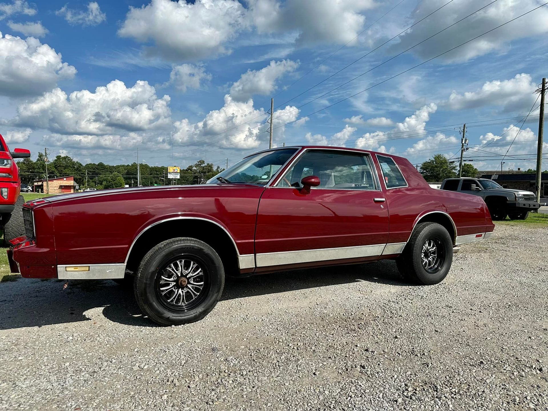A red car is parked in a gravel lot.