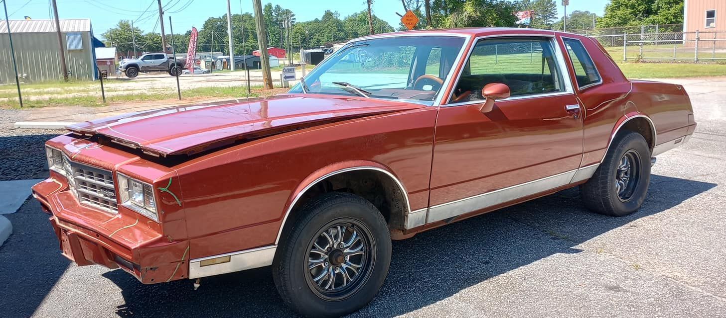 A red car with a broken hood is parked on the side of the road.