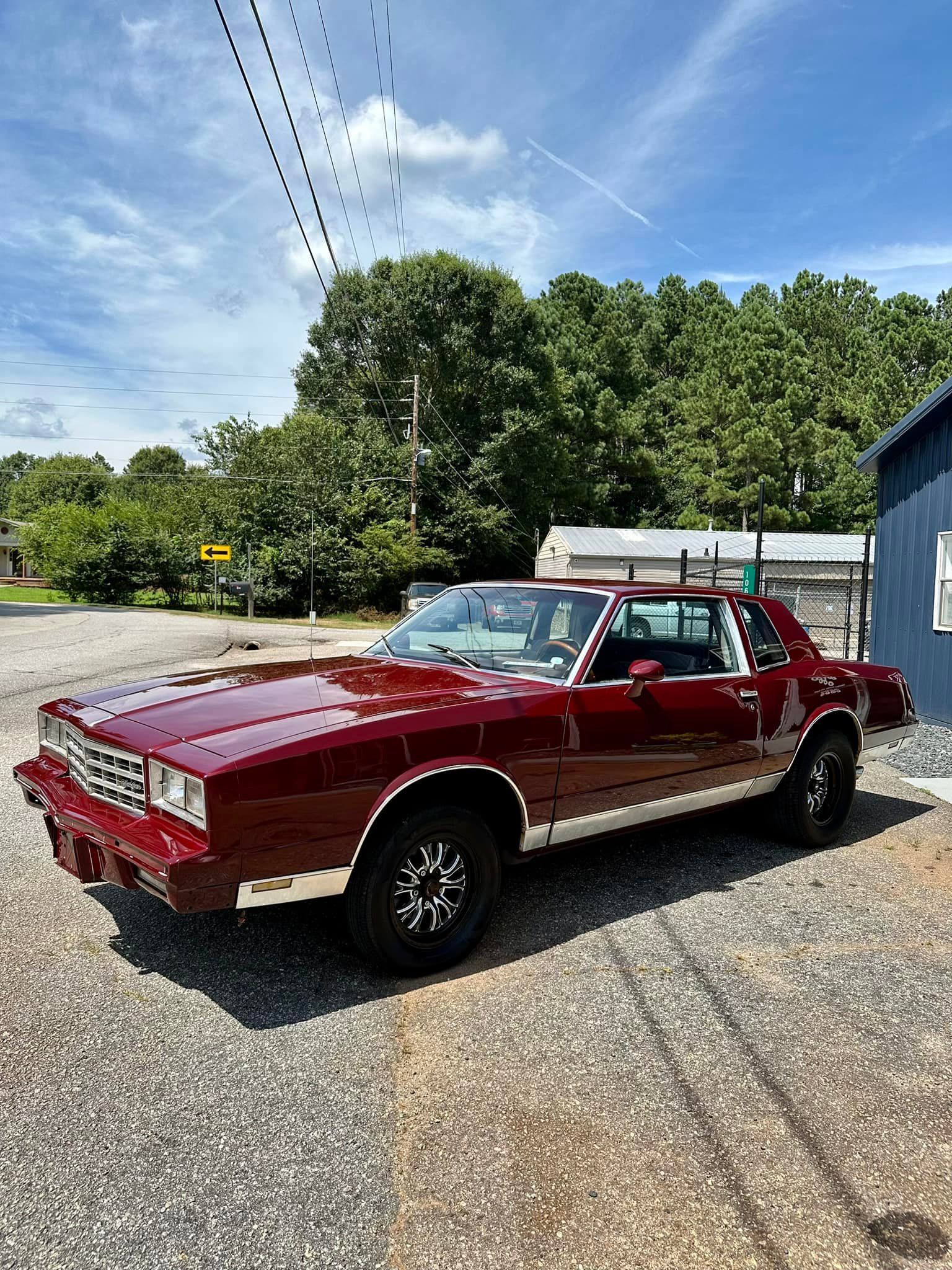 A red car is parked in a gravel lot in front of a building.
