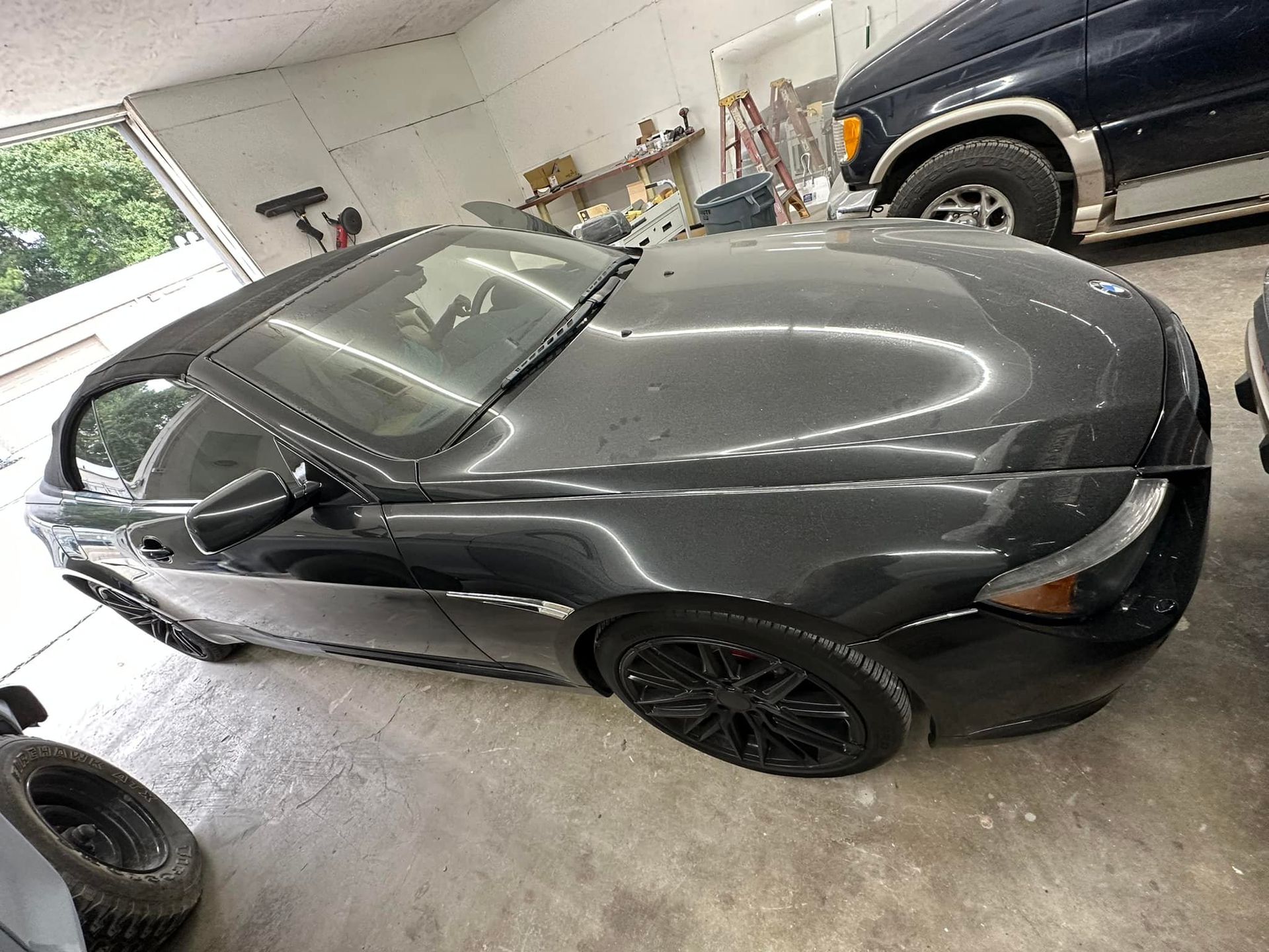 A black car is parked in a garage next to a truck.