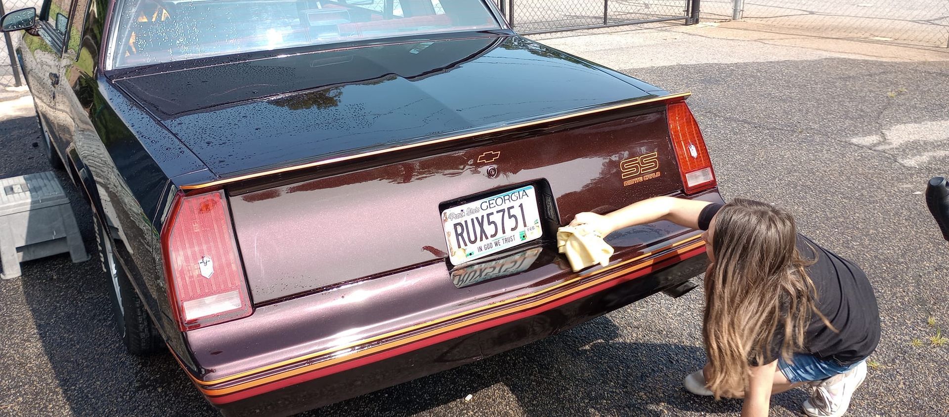 A woman is cleaning the back of a car with a towel.