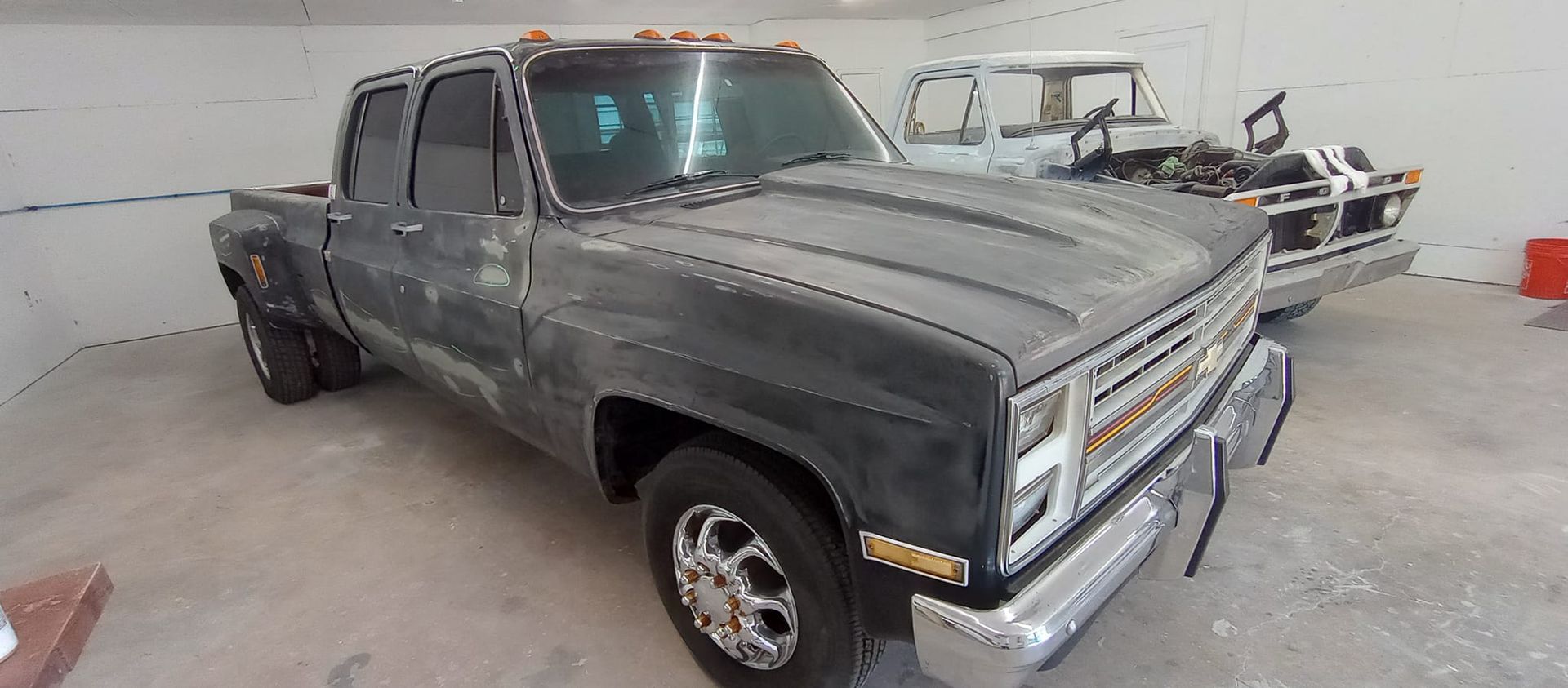 A gray truck is parked in a garage next to another truck.