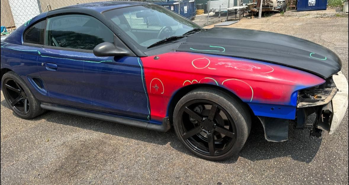A blue and red mustang is parked on the side of the road.