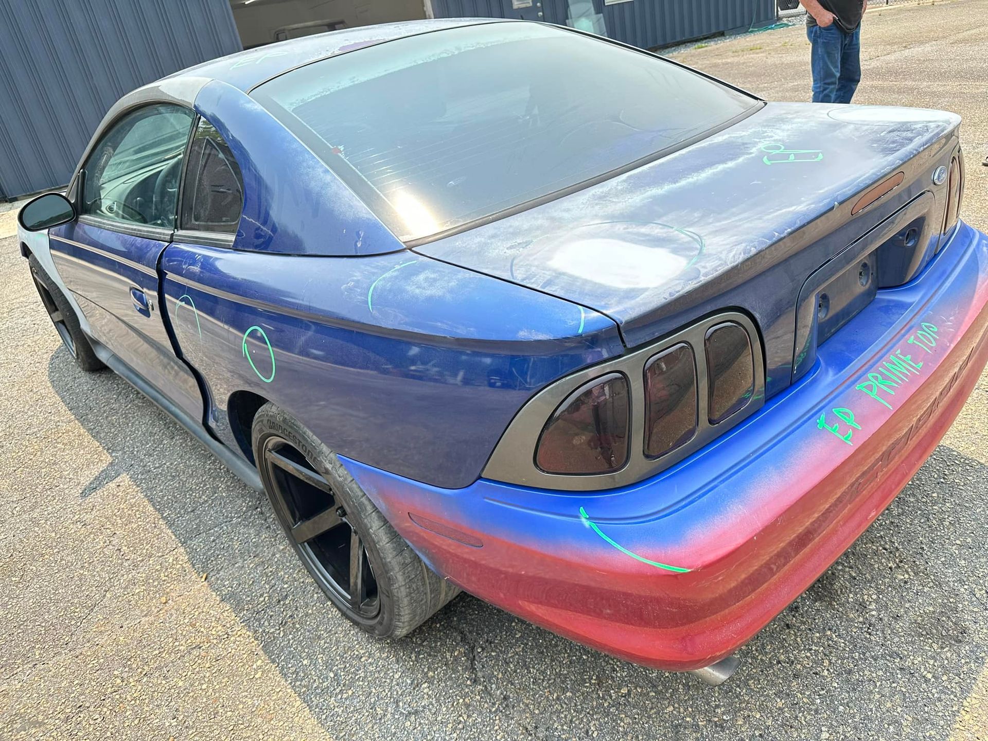 A blue and red mustang is parked on the side of the road.
