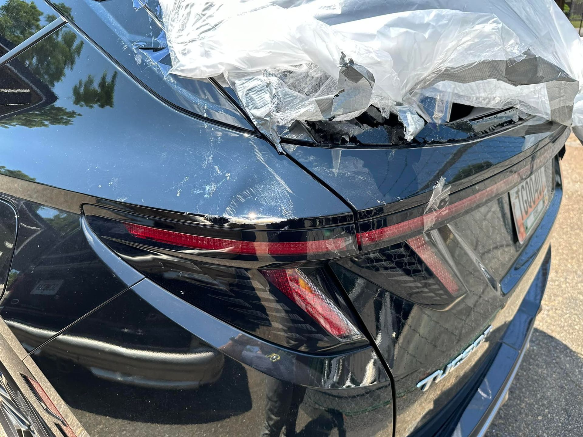 The rear end of a black car is wrapped in plastic.