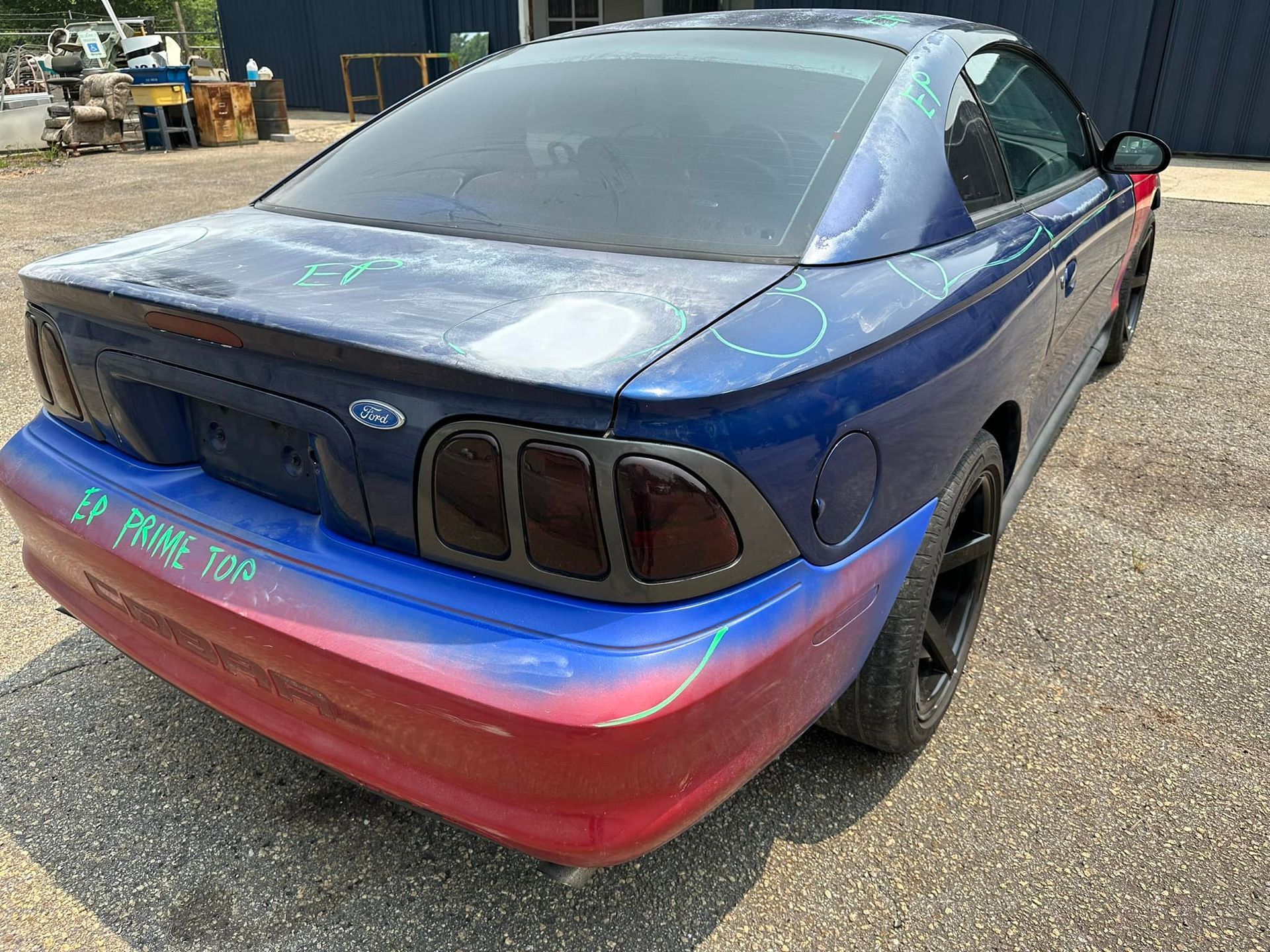 A blue and red ford mustang is parked in a gravel lot.