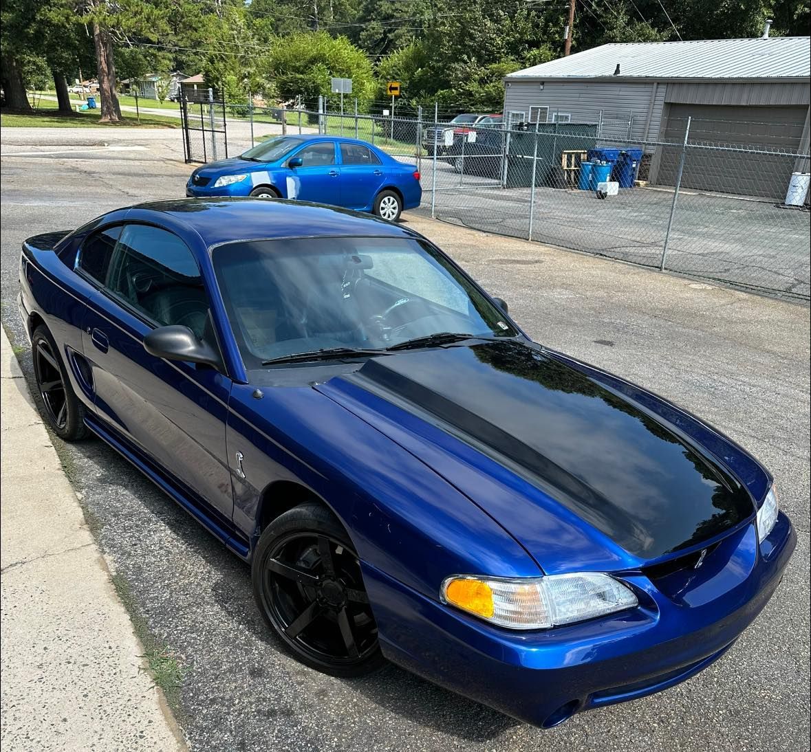 A blue car with a black hood is parked on the side of the road