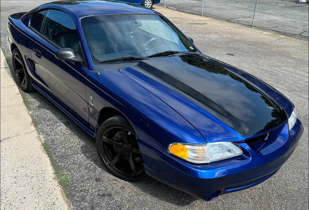A blue mustang with a black hood is parked on the side of the road.