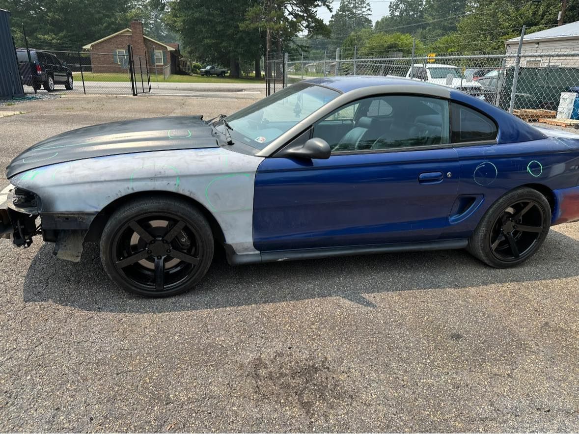 A blue and white mustang is parked in a gravel lot.