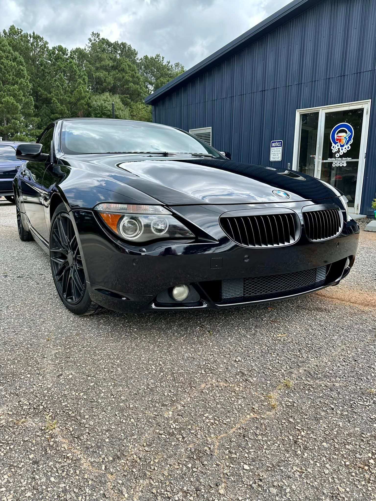 A black bmw 6 series is parked in front of a blue building.