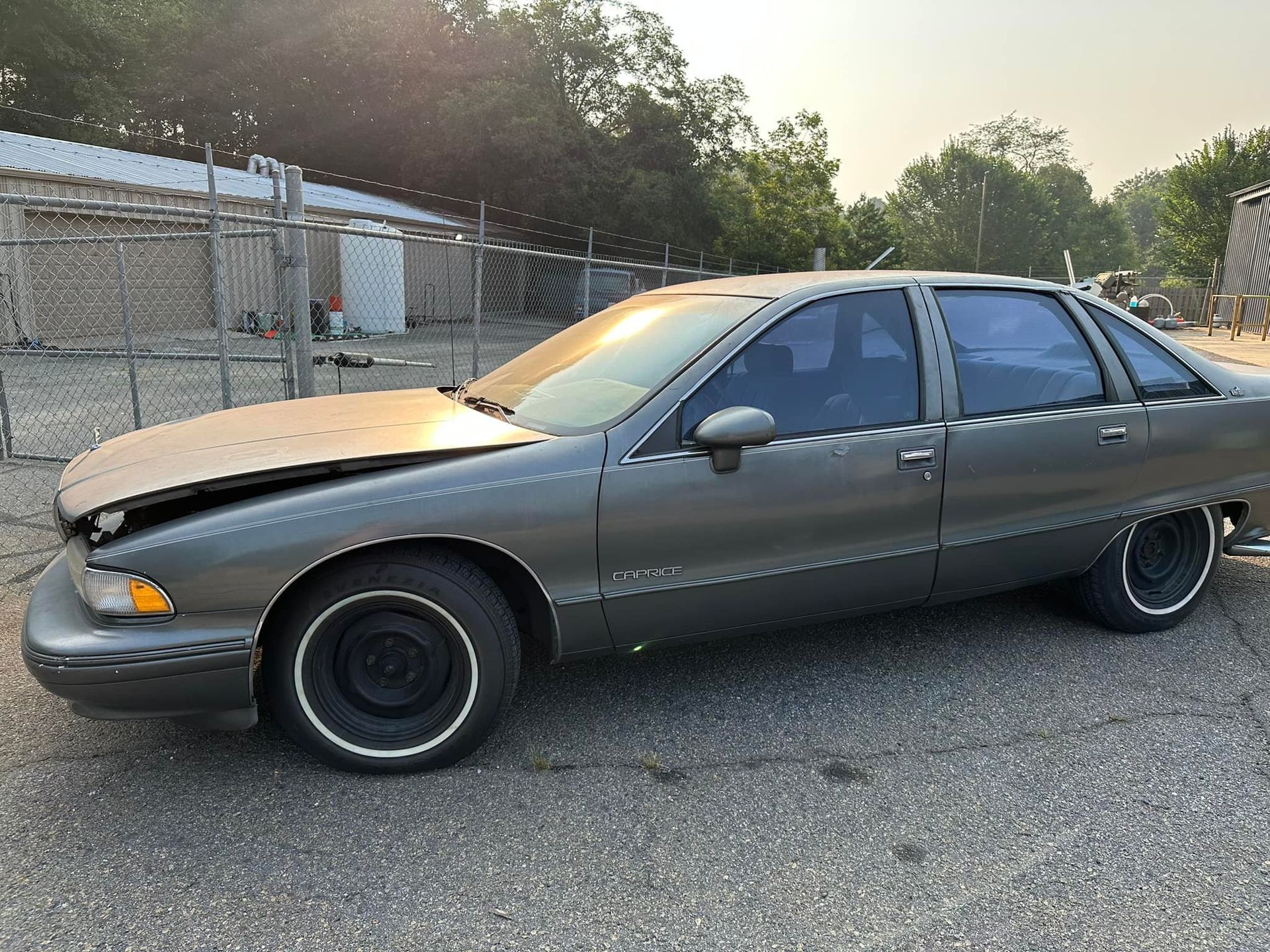 A gray car with a broken hood is parked in a parking lot.