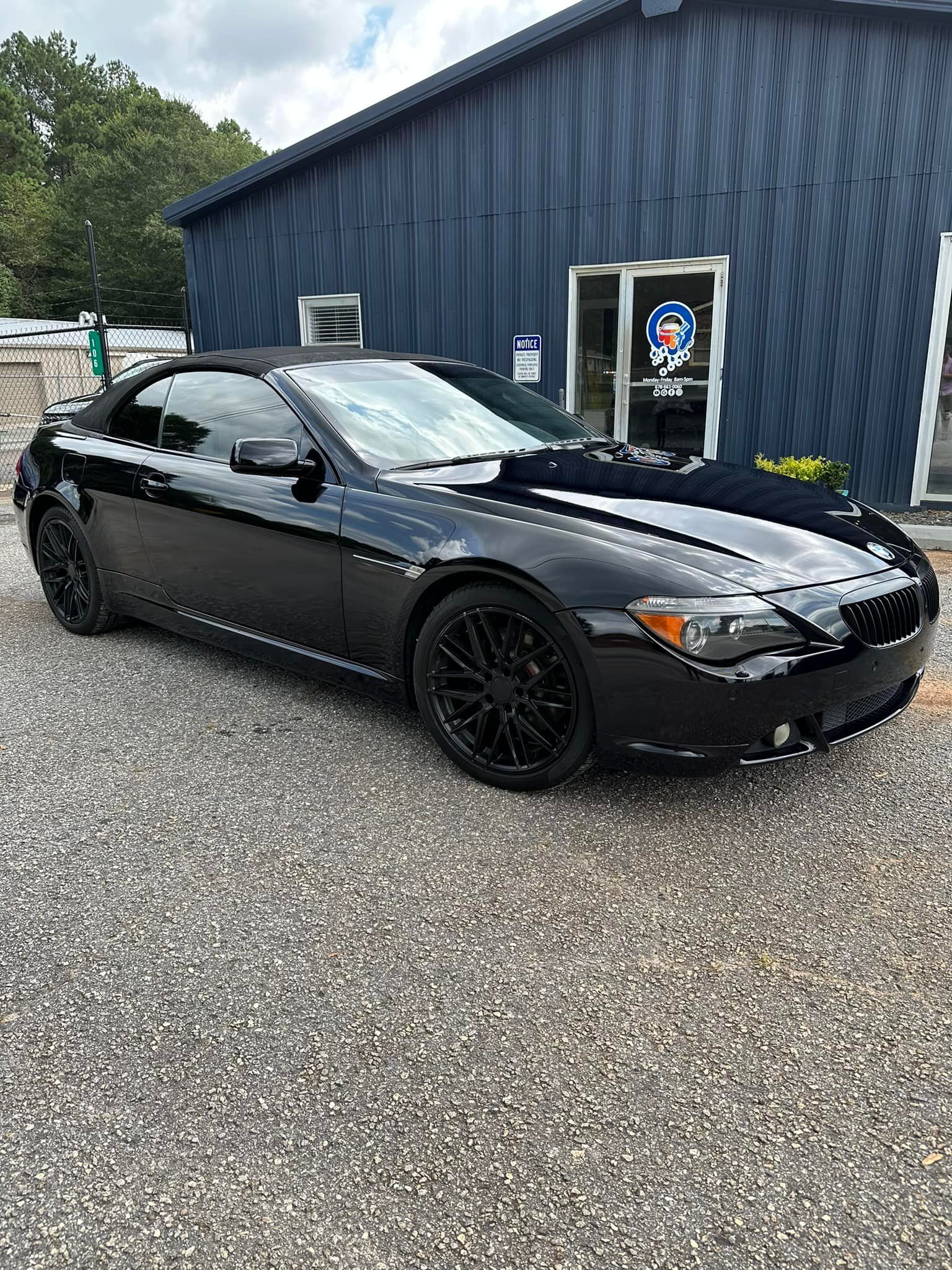 A black bmw 6 series convertible is parked in front of a building.