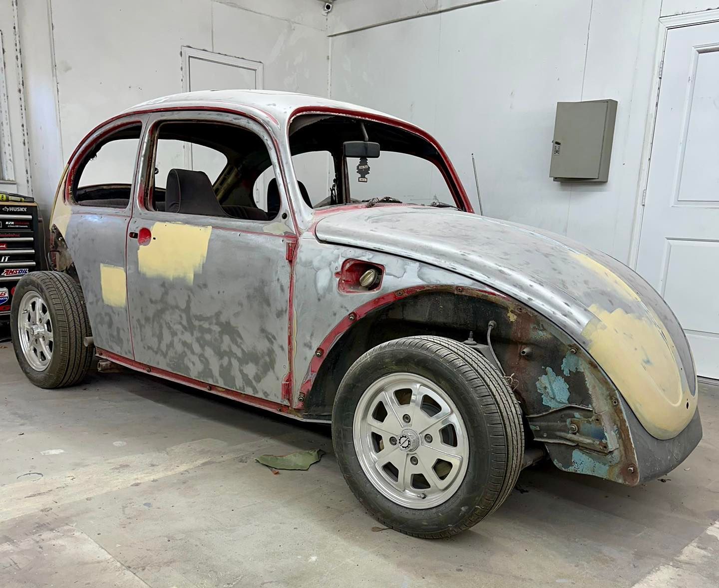 A volkswagen beetle is being restored in a garage.